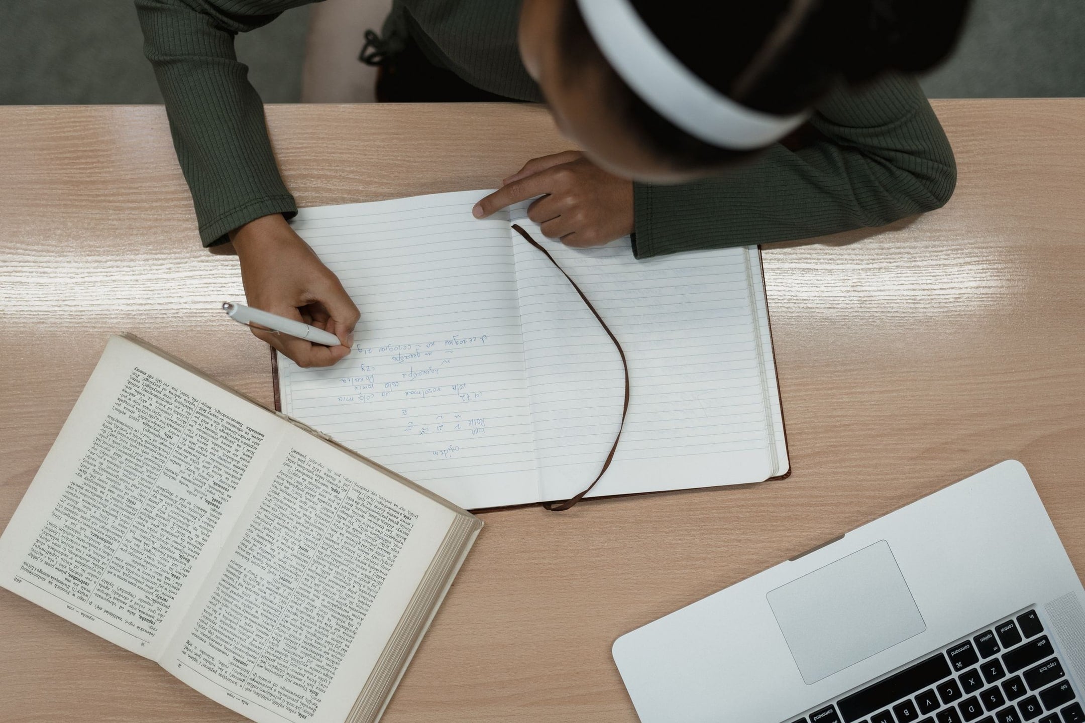 A student studies at a desk with an open textbook, notebook and laptop.